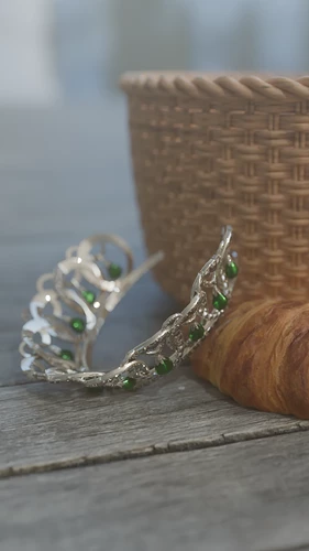 A diamond and emerald tiara fallen onto a wooden platform beside a croissant and a woven basket whose contents we cannot see. I'm sure everything's fine.